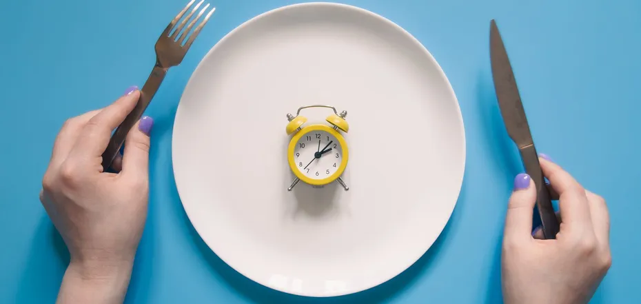 life hands holding knife and fork above alarm clock on a plate on blue