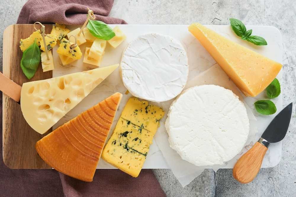 Set or assortment cheeses Maasdam, smoked cheese, camembert, blue cheese, parmesan, brie cheese with basil and pepper on on white marble board white wooden old background Top view Free copy space