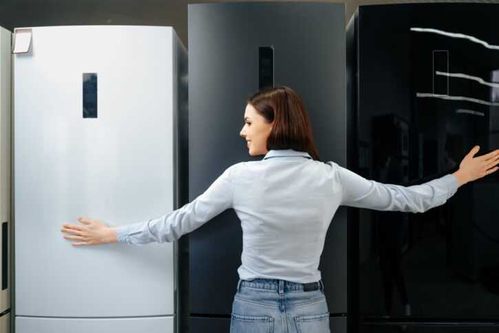 Young happy woman leaning on her new refrigerator in a shopping mall