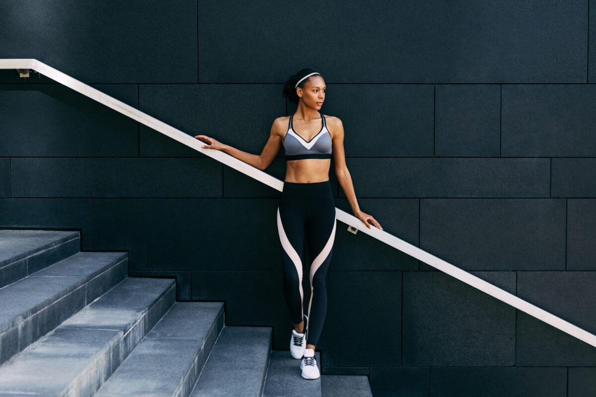 Woman in sportswear relaxing after workout, standing on staircase