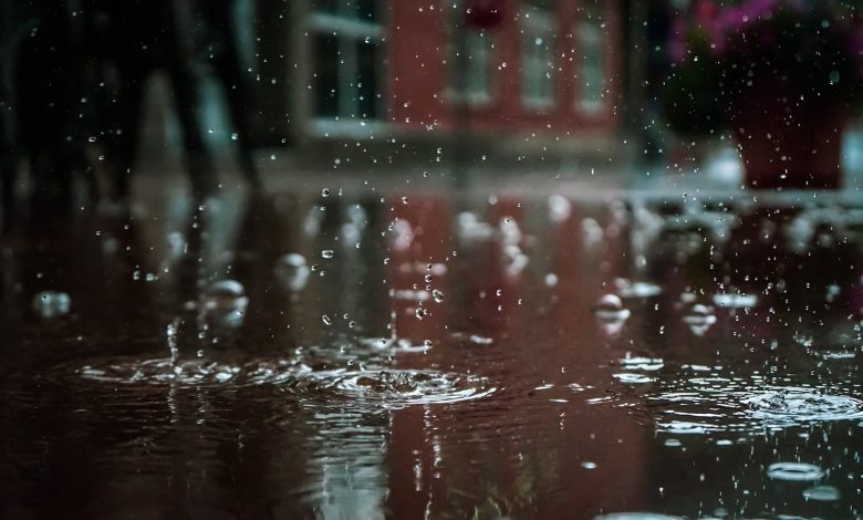 Close-up of raindrops splashing into a puddle, capturing reflections and textures in an outdoor urban setting.