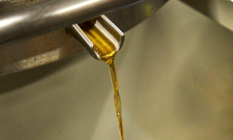 Golden oil pouring from a metal spout into a container