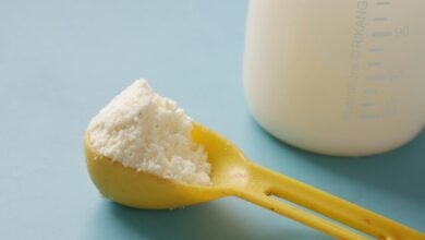A yellow spoon filled with powdered milk, next to a measuring bottle, on a blue background.