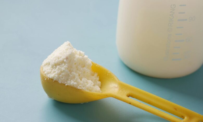A yellow spoon filled with powdered milk, next to a measuring bottle, on a blue background.