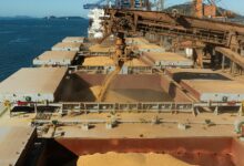 Aerial view of a cargo ship loading grain at a bustling industrial port by the sea.
