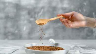 A close-up of a hand pouring flaxseeds into a bowl using a wooden spoon.
