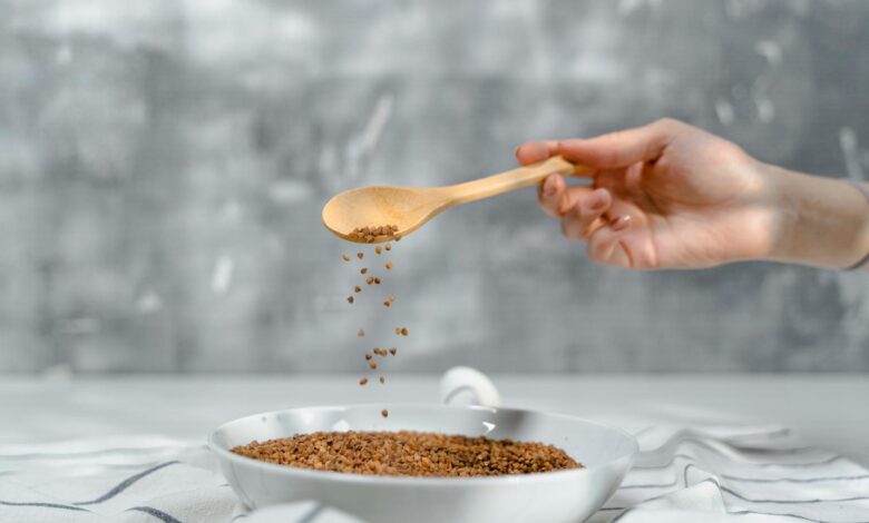 A close-up of a hand pouring flaxseeds into a bowl using a wooden spoon.