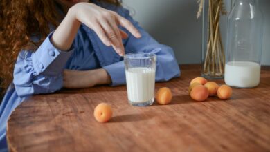 A serene still life of apricots and a glass of milk on a wooden table with a woman's hand.