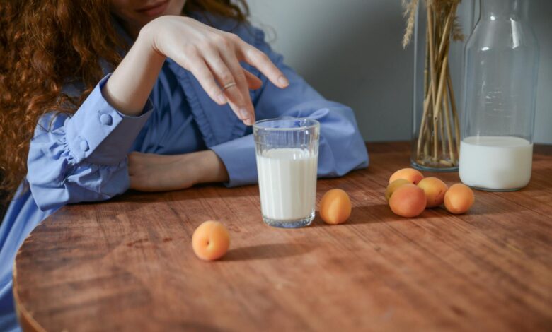 A serene still life of apricots and a glass of milk on a wooden table with a woman's hand.