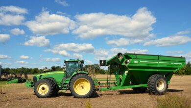 Green tractor pulling a large grain cart in a field.