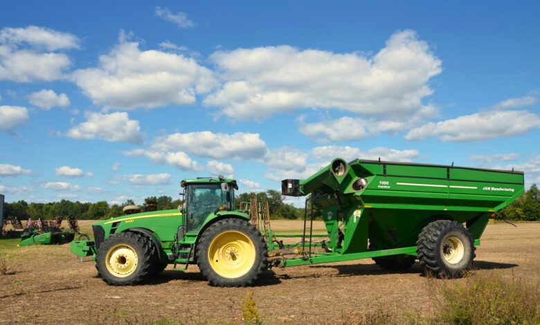 Green tractor pulling a large grain cart in a field.