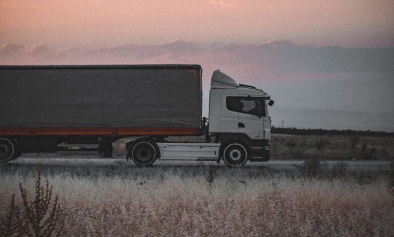 A cargo truck travels on a highway at sunset, surrounded by an open landscape, symbolizing logistics and transportation.