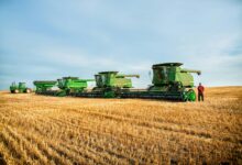 a man standing in a field next to a row of green farm equipment