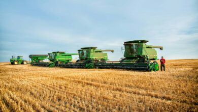 a man standing in a field next to a row of green farm equipment