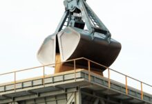 Clamshell grab unloading bulk cargo at an industrial port terminal.
