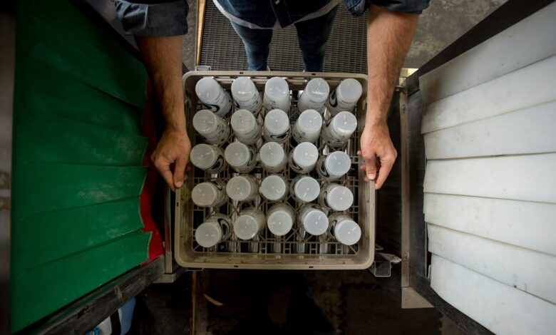 person in black shirt and blue denim jeans standing in front of white plastic bottles